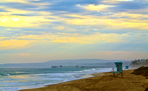 A scenic beach with soft waves and a vibrant rainbow arching across a clear blue sky.