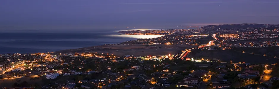 A city aglow with nighttime lights, featuring the ocean in the distance.
