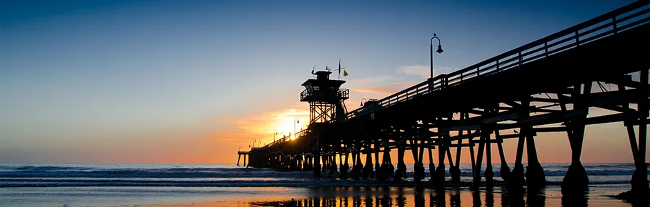 A scenic pier with a lighthouse silhouetted against a vibrant sunset sky.